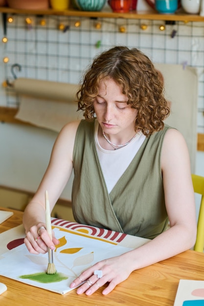 Diligent and creative girl in casualwear holding paintbrush over paper