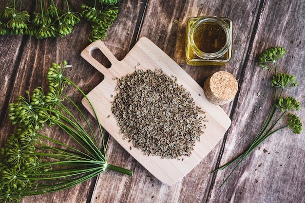 Dill flowers and dry seeds Anethum graveolens essential cosmetic oil in bottle on wooden background overhead flat lay