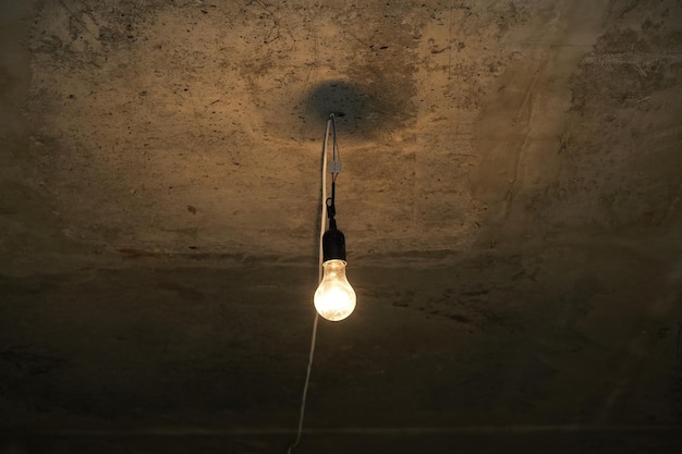 Dim light bulb on concrete ceiling of basement or bomb shelter. Electric lamp. Temporary lighting.