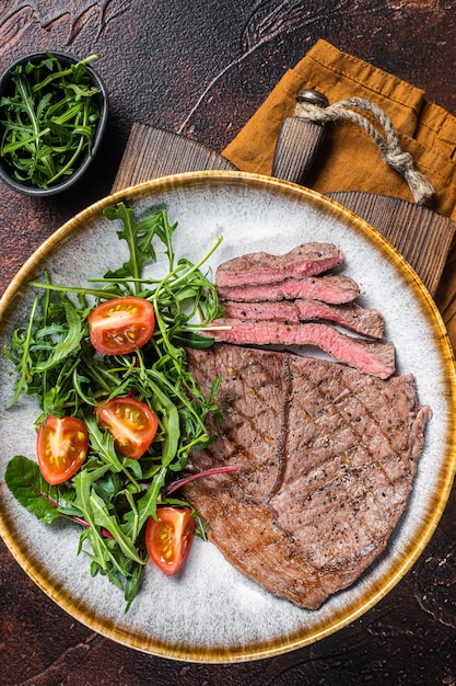 Diner with grilled beef veal meat steaks and vegetable salad. Dark background. Top view.