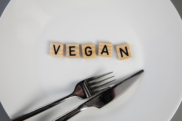 Dining plate with fork and knife with the text vegan concept of dieting vs healthy veganismvegetaria