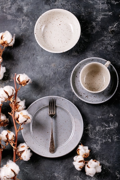 Dinner place setting. A blue modern ceramic plate with silver fork decorated with cotton flower over dark texture surface. Top view, flat lay. 