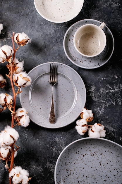 Dinner place setting. A blue modern ceramic plate with silver fork decorated with cotton flower over dark texture surface. Top view, flat lay. 