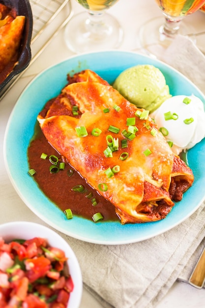 Dinner plate with Chicken enchiladas garnished with green onions and sour cream.