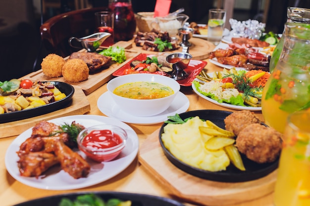 Dinner table with meat grill, roast new potatoes, vegetables, salads, sauces, snacks and lemonade, top view.