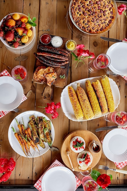 Dinner table with meat grill, sausages, corn, roast vegetables, sauces, snacks and lemonade, top view, family dinner or lunch, eating concept