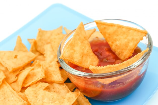 Dipping tortilla chips with salsa sauce in dish on white background