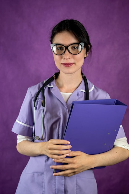 Direct view of doctor intern girl with books in hands in gown isolated plain studio background