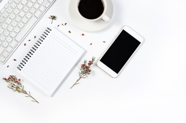 Directly above shot of mobile phone with black coffee and spiral notebook over white background