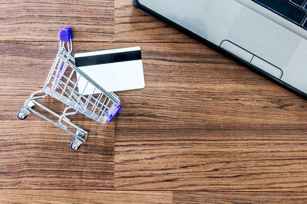 Photo directly above small shopping cart with credit card by laptop on table