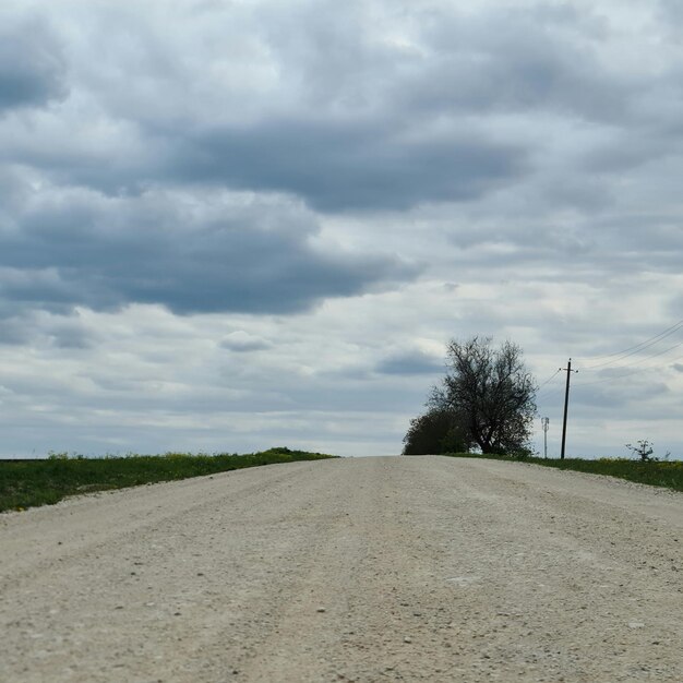 A dirt road is shown with a cloudy sky in the background.