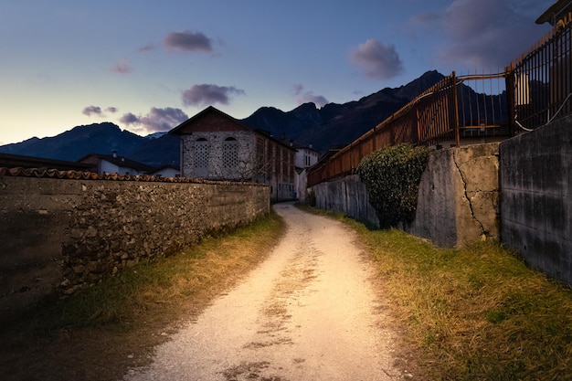 Dirt road between old houses at sunset, mountains in the background, Santa Giustina, Belluno