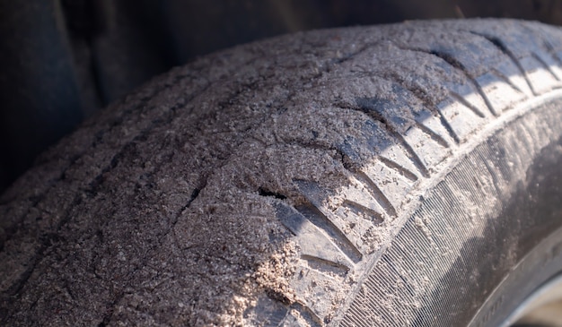 Dirty car wheel on a soil road to the countryside. Close-up detail of a tire. Transport, driving and car concept. The car got stuck in the sand.