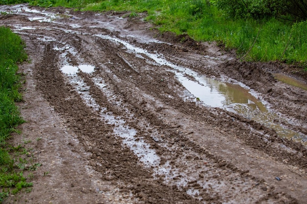 Dirty clay mud road with puddles and tire tracks closeup with selective focus and linear perspective