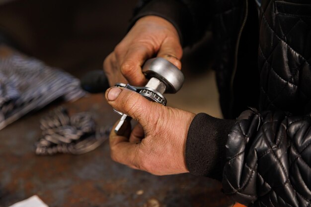 Dirty hands of caucasian car technician holding silver adjustable oil filter wrench closeup with selective focus