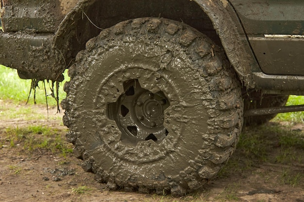 Dirty offroader wheel is standing on the road with the ground