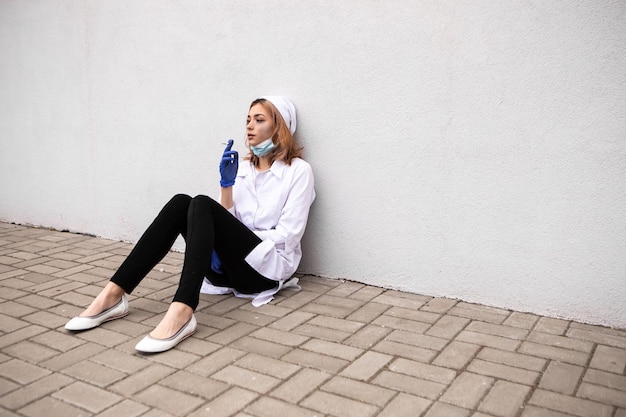 Photo dirty tired nurse with ash on face sitting outside hospital and smoking