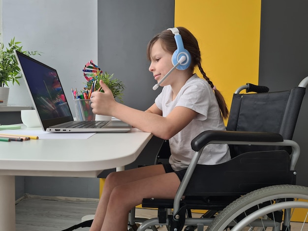 Disabled child girl in headphones with microphone and laptop works at home