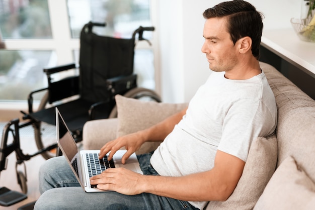 Disabled Man Sitting on Sofa and Typing on Lap.