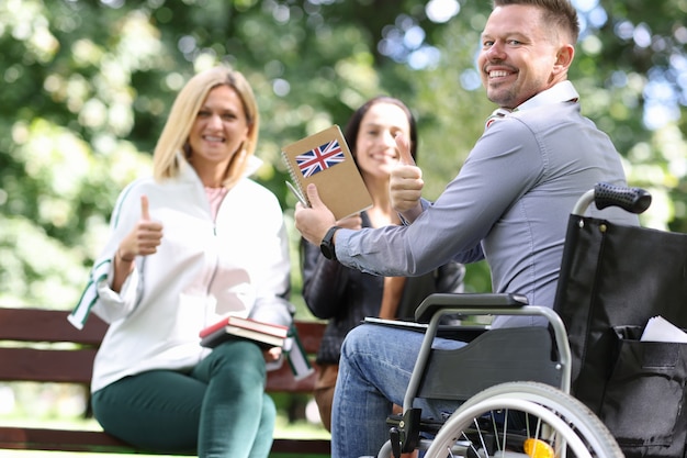 Disabled man in wheelchair is studying english with girlfriends in park communication and