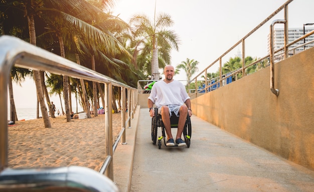 Disabled man in a wheelchair moves on a ramp to the beach.