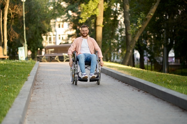 Disabled man in wheelchair rides on a path in park