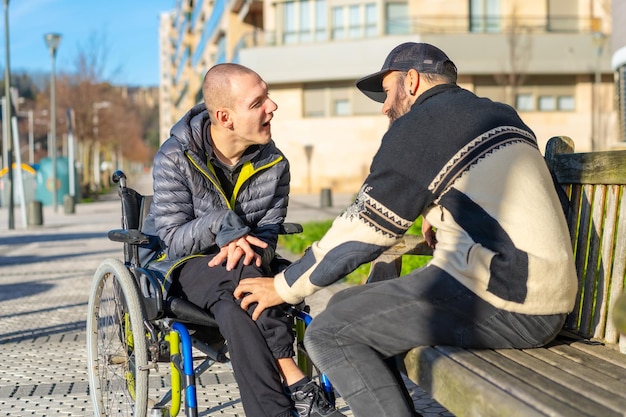 A disabled person in a wheelchair with a friend sitting down having fun normality for the disabled