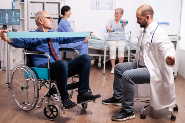 Disabled senior man being assisted by physical therapist by doctor in modern heathcare facility