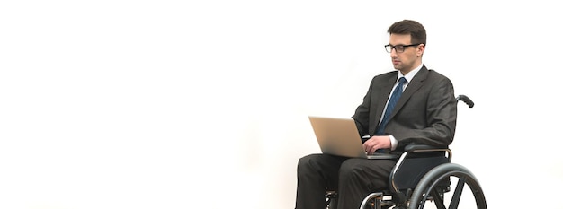 The disabled in the wheelchair works with a laptop on the white wall background