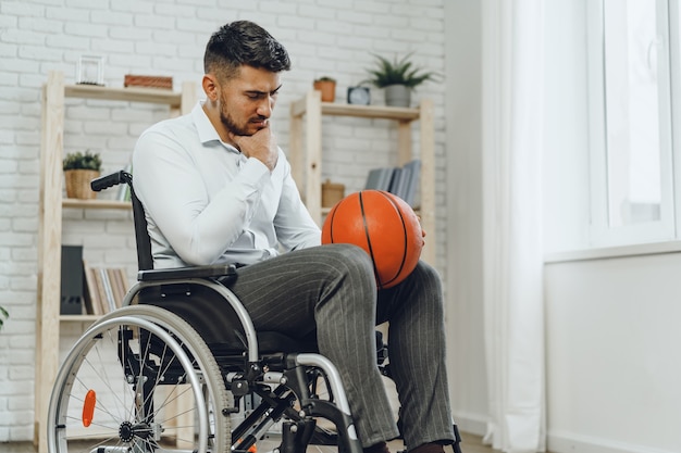 Disabled young man in wheelchair holding basketball ball indoors