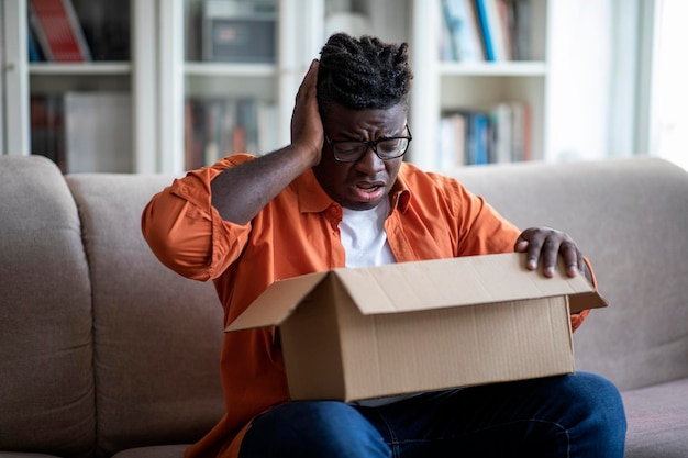 Disappointed african american young guy customer opening parcel box