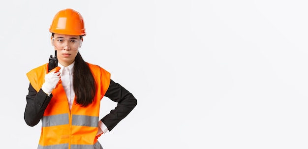 Disappointed asian female construction engineer technician or industrial manager in safety uniform calling employee via walkietalkie scolding personal using radio communication at enterprise