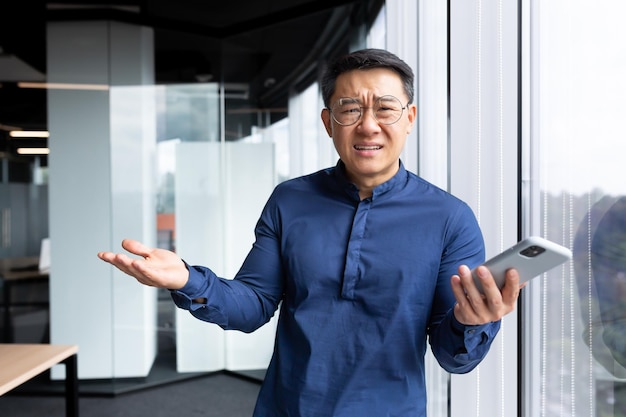 Disappointed man inside office standing near window portrait of upset asian man inside office with