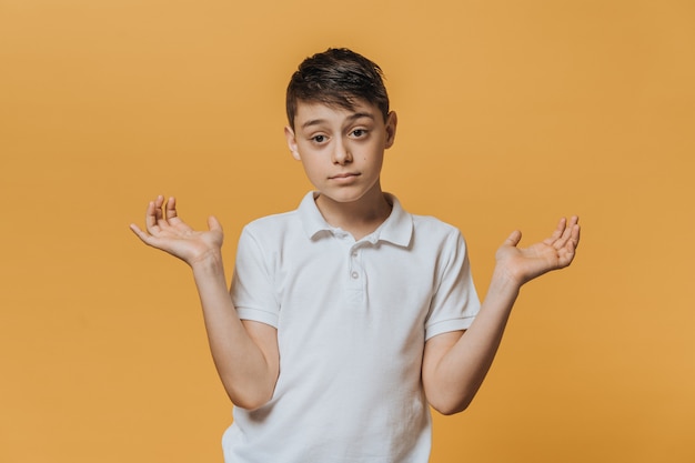 Disappointed young boy in a white t-shirt spreads his hands in doubt mood. Sincere people emotions.