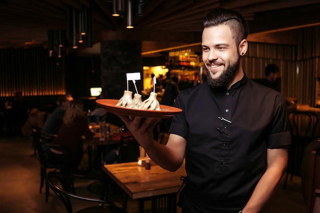 A discerning waiter in black clothes, with a beard and a portion of khinkali