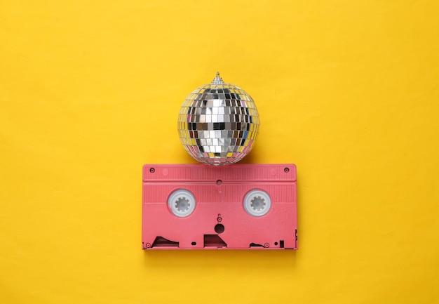 Disco ball with retro video cassette on yellow background Minimalism party concept