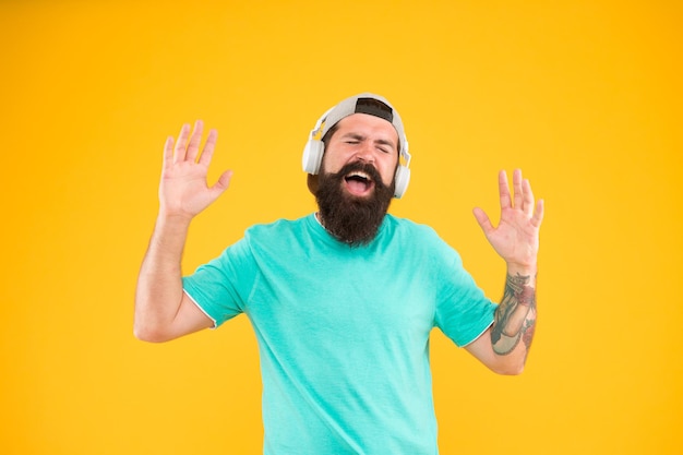 Disco sound Bearded man relaxing with melodious sound on yellow background Hipster wearing earphones playing electronic sound Brutal guy listening to sound track in headset