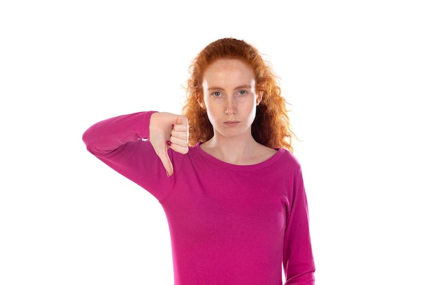 Discontent young redhead girl wearing pink tshirt over white background shows disapproval sign keeps thumb down