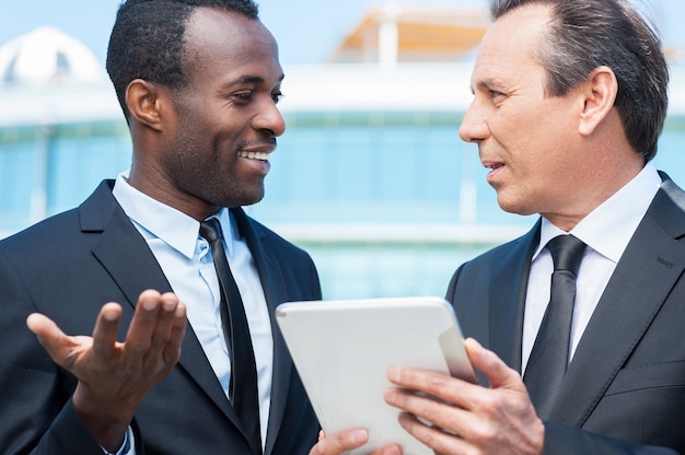 Discussing business. Two cheerful business men talking outdoors while one of them holding digital tablet