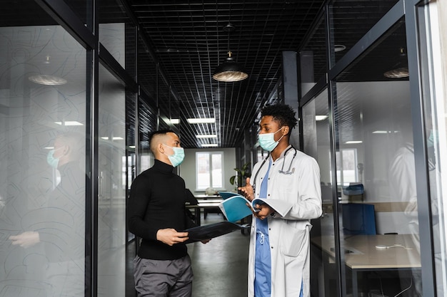 Discussion and consultation between black doctor and patient in medical clinic African surgeon treats Asian handsome man