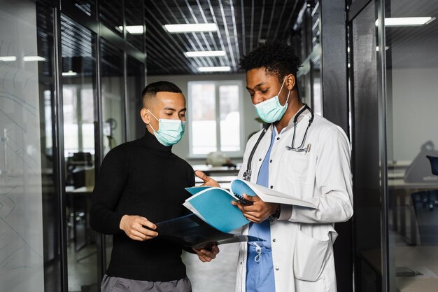 Discussion and consultation between black doctor and patient in medical clinic African surgeon treats Asian handsome man