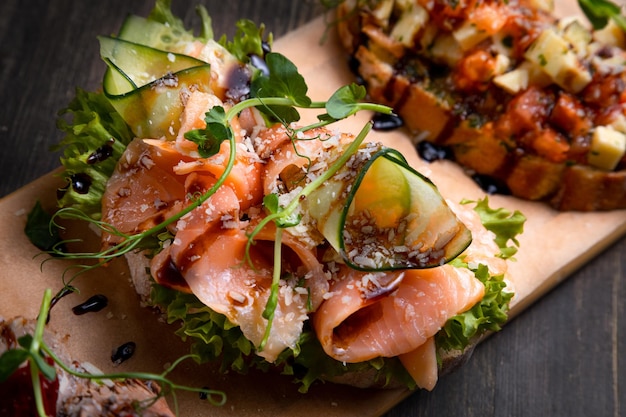 A dish of 3 different tapas stuffed with meat fish and various microgreens served on a board against a dark background