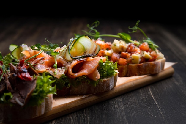 A dish of 3 different tapas stuffed with meat fish and various microgreens served on a board against a dark background