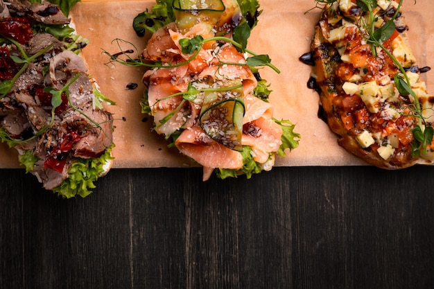 A dish of 3 different tapas stuffed with meat fish and various microgreens served on a board against a dark background