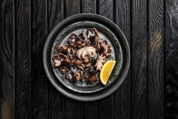 A dish of cooked baby octopus with a slice of lemon shot from above dark wooden backdrop