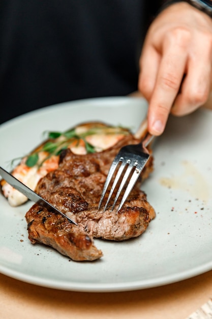 Dish plate with meat steak on the bone in the restaurant man cuts ready juicy meat steak