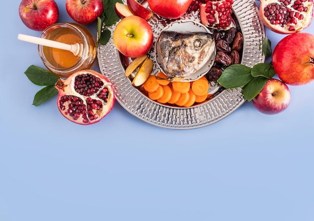 A dish with a New Year's treat for the holiday Rosh Hashanah pomegranate honey dates apple slices and carrots Blue background A copy space