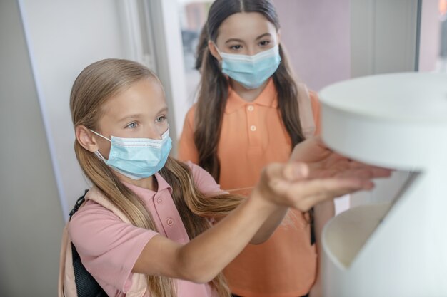 Disinfection. Fair-haired girl in preventive mask getting some sanitizer into her hand