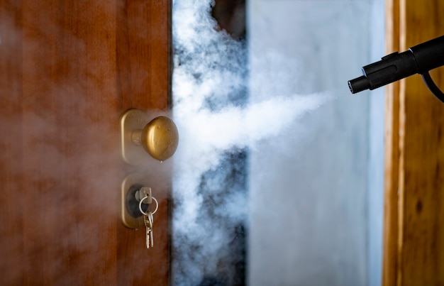 Disinfection and sanitization with steam at home, steam flow is directed to the door handle and keys in the lock