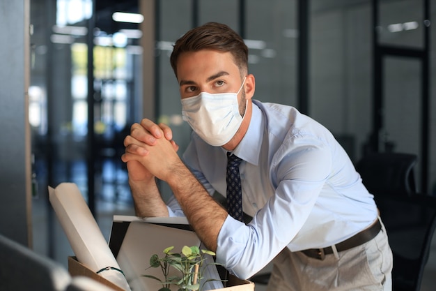 Dismissal employee in an epidemic coronavirus. Sad dismissed worker are taking his office supplies with him from office.